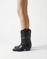 Bota de cuero negro estilo texano, con taco bajo y punta fina. Incluye un aplique desmontable en la zona del empeine decorado con tachas metálicas y flecos largos.
