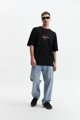 Remera negra de manga corta con corte oversize y cuello redondo. Presenta un estampado pequeño en la espalda con texto en naranja y blanco que dice "Free Spirits Freedom & Waves All Day / Every Day".