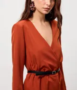 Enterito sastrero color terracota con escote en V profundo, mangas largas con puños rectos y corte evasé. Incluye un cinturón fino negro removible para ajustar la cintura y cierre posterior.