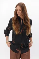 Camisa color crema de tela sedosa bordada con lentejuelas y botones negros a contratono, de corte clásico y mangas largas.