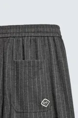 Pantalón de corte baggy fit, color gris oscuro con estampado de rayas verticales finas. Presenta cintura elástica con cordón interior, bolsillos frontales de vivo y bolsillos traseros de plastrón.