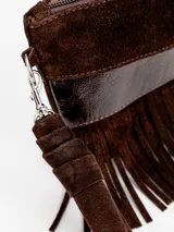 Sobre de mano confeccionado en gamuza marrón, con diseño de flecos colgantes, franja de cuero texturizado, cierre superior y correa de muñeca desmontable.