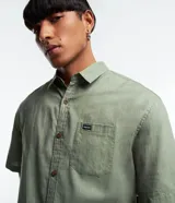 Camisa de corte relajado para hombre, confeccionada en una mezcla de cáñamo y algodón. Presenta cuello inglés, manga corta, cierre frontal con botones y un bolsillo en el pecho con una pequeña etiqueta aplicada.