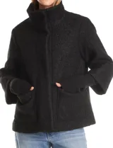 Tapado de tejido boucle color verde oscuro, con silueta evasé y largo a la cadera. Presenta cuello alto envolvente, cierre frontal con botones a presión ocultos y bolsillos frontales de gran tamaño. Cuenta con mangas 3/4 de corte amplio y puños de tejido rib al tono que se extienden para cubrir las muñecas.