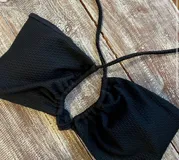 Top de bikini negro con tiras finas cruzadas en el frente y broche de tres posiciones en la espalda.