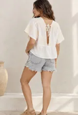 Blusa blanca de corte amplio y corto, con escote en V y mangas cortas. Presenta detalles de bordados florales en los hombros y mangas, además de ribetes con terminación de pompones pequeños.