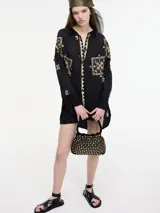 Camisa negra de manga larga con cuello camisero y bordados geométricos en hilo dorado. Presenta un borde en zigzag dorado en la abertura frontal y un largo irregular en la espalda.