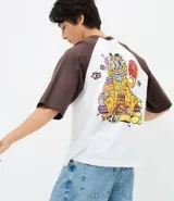 Remera de algodón con diseño estilo baseball, cuerpo blanco y mangas cortas en color marrón oscuro. Presenta un estampado gráfico colorido en la espalda con el personaje Garfield rodeado de comida y elementos decorativos.