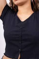 Remera de morley negra, entallada, con cuello en V y cierre frontal con botones. Presenta mangas cortas con terminación ondulada.