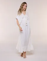 Vestido largo blanco confeccionado en viscosa con hilos de lurex, escote en V profundo con lazo y borlas, mangas kimono y falda fluida con volados en el ruedo.