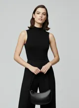 Bolso de hombro negro de efecto cuero, con forma curva y cierre de cremallera. Presenta costuras decorativas en el cuerpo y correa ajustable para llevar al hombro.