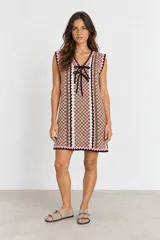 Vestido corto de punto sin mangas con diseño de damero en tonos rosado, verde y blanco, escote en V con cordones negros para ajustar y detalles de rayas verticales.