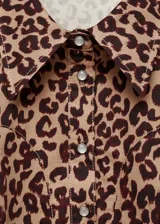 Vestido corto estilo camisero con estampado de leopardo, cuello camisero, cierre frontal con botones y mangas largas con puños abotonados.