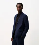 Saco de traje azul marino, de corte formal, con solapas de muesca, cierre de dos botones frontales y bolsillos con solapa.