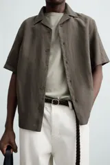 Camisa de lino color negro con calce relajado, cuello bowling y manga corta. Presenta cierre frontal con botones a tono y aberturas laterales en el bajo.