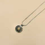 Collar con dije circular de San Benito, elaborado en una combinación de plata y oro. El dije presenta un diseño detallado con acabado envejecido y una pieza central dorada. La cadena es de tipo soga con eslabones metálicos.