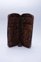 Billetera chica de cuero negro con textura tipo cocodrilo, cierre exterior, bolsillo para monedas con cierre en la parte trasera, múltiples ranuras para tarjetas y billetes, y forro rojo.