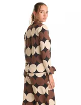 Conjunto de dos piezas compuesto por camisa de manga larga con nudo frontal y pantalón estilo palazzo de pierna ancha. Ambas prendas presentan un estampado geométrico de círculos grandes en tonos marrón, negro y beige. La camisa cuenta con cuello solapa y cierre frontal con botones, mientras que el pantalón posee tiro alto y corte holgado.