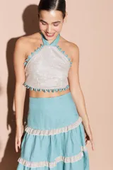 Top halter color plateado brillante con tiras turquesas y detalles de mini ojalillos turquesas en el escote y el dobladillo. Espalda descubierta.