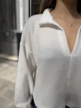 Buzo blanco de corte holgado con cuello polo y cierre frontal parcial. Presenta mangas largas amplias y un diseño de silueta relajada, confeccionado en tejido suave.