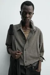 Sobrecamisa de corte cropped confeccionada en tejido ligero con algodón, con estampado de cuadros pequeños en tonos oscuros. Presenta cuello solapa, cierre frontal de botones, manga larga con puño abotonado y bajo con elástico en la espalda.