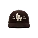 Gorro tipo dad hat color negro con bordado frontal en color crudo con las letras 'LA' en el centro y las frases 'Mi CASA' y 'Su CASA' a los lados.