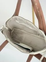 Cartera bandolera de cuero color crema con doble asa de mano marrón y correa larga de cinta con logo.