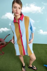 Túnica de algodón con diseño de rayas verticales multicolor en tonos celeste, marrón y fucsia. Presenta cuello polo, manga corta y cierre frontal con botones.