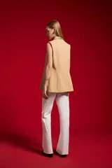 Chaleco sastrero de poliéster color beige, con solapa ancha, doble botonadura frontal y bolsillos de ribete simulados.