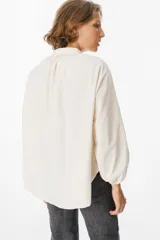 Camisa de pana color verde oliva, con cuello mao, cierre frontal de botones y mangas largas abullonadas con puños elásticos.