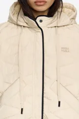 Chaleco acolchado color crema con capucha integrada, cierre frontal de botones a presión y vivos en contraste color negro. Presenta diseño de costuras geométricas y bolsillos laterales.