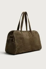 Bolso de viaje de diseño minimalista confeccionado en piel con acabado serraje. Cuenta con compartimento principal con cierre de cremallera e imanes, interior con bolsillos organizadores y doble asa de mano en piel.