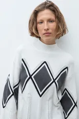 Media polera de tejido de punto color crudo, con diseño de rombos en el frente en tonos gris y negro. Presenta cuello alto y mangas largas.