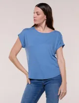 Remera blanca de punto acanalado, con escote redondo adornado con tachas metálicas, mangas cortas estilo japonesa con dobladillo y ruedo curvo.