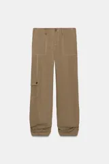 Pantalón de tiro medio confeccionado en tejido fluido color tostado. Presenta bolsillos de plastrón en el delantero y en la pierna, solapas en la espalda y detalle de frunces ajustables en el bajo. Cierre frontal con cremallera y botón.