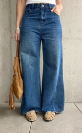 Jean wide leg de tiro medio-alto, color azul con lavado clásico y efecto desgastado. Presenta costuras laterales destacadas que estilizan la silueta, bolsillos delanteros y traseros, y cierre frontal con botón metálico y cremallera.