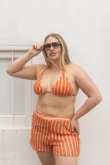 Conjunto de bikini de lycra color naranja con rayas verticales blancas. El corpiño es de corte triangular con tirantes finos y la bombacha es tipo colaless con tiras laterales ajustables.