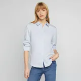 Camisa de corte ajustado en color azul claro, con cuello italiano, cierre frontal de botones y mangas largas con puños abotonados.