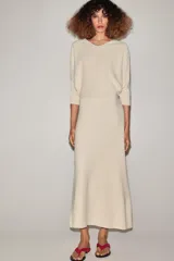 Vestido midi de punto color marfil con escote en V, mangas largas de sisa ancha, cintura entallada y falda de corte evasé.