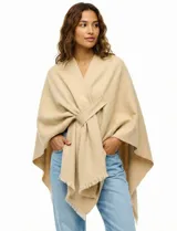 Ruana de tejido soft color beige, con cuello en V y un lazo o pasador frontal para ajustar. El ruedo tiene terminación desflecada.