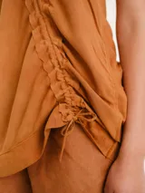 Blusa sin mangas color tostado, de corte holgado y asimétrico, con detalle fruncido diagonal.
