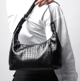 Cartera tipo baguette de cuero sintético color negro, con diseño curvo, cierre superior y asa corta regulable con hebilla metálica.