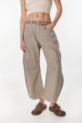 Pantalón de denim modelo Jean Kai, color camel con costuras contrastantes en blanco. Presenta tiro medio, diseño holgado de piernas anchas con pinzas en las rodillas y presillas para cinturón. Incluye un cinturón delgado de cuero marrón con hebilla metálica.