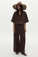 Pantalón de lino marrón de corte ancho y relajado, con pinzas frontales, bolsillos y lazo ajustable en la cintura.
