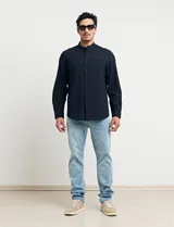 Camisa de cuello mao y manga larga, confeccionada en una mezcla de lino y algodón. Presenta un diseño de corte recto con botones en tono natural y un bolsillo pequeño en el pecho.