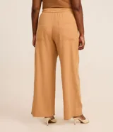 Pantalón de sarga de corte ancho tipo pantalona, color tostado, con cintura fija, trabillas, elástico trasero y cinturón incorporado con hebilla redonda.