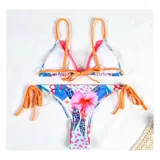 Bikini de dos piezas con estampado floral y tropical. El corpiño es de estilo triangular con bordes decorativos y tiras regulables. La bombacha es de corte tanga con tiras laterales ajustables.