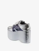 Zapatilla deportiva con plataforma extragrande, color plateado metálico con efecto arrugado en la plataforma y acabado brillante en el cuerpo. Presenta tres franjas laterales en azul marino brillante y cordones azules.