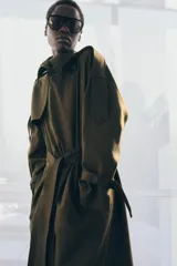 Trench oversize de Zara Woman Collection, color verde militar, con cuello solapa, cierre frontal cruzado con botones y cinturón ajustable del mismo tejido. Presenta mangas largas con trabillas ajustables y bolsillos delanteros.