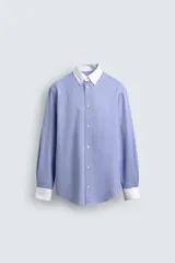 Camisa de corte regular fit confeccionada en tejido ligero de algodón, con diseño de rayas verticales azules y blancas. Presenta cuello abotonado y puños en color blanco a contraste, con cierre frontal de botones.